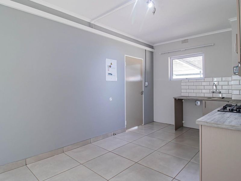 A clean, modern kitchen featuring a gas hob, subway tile backsplash, stainless steel sink, and neutral cabinetry with tiled flooring.