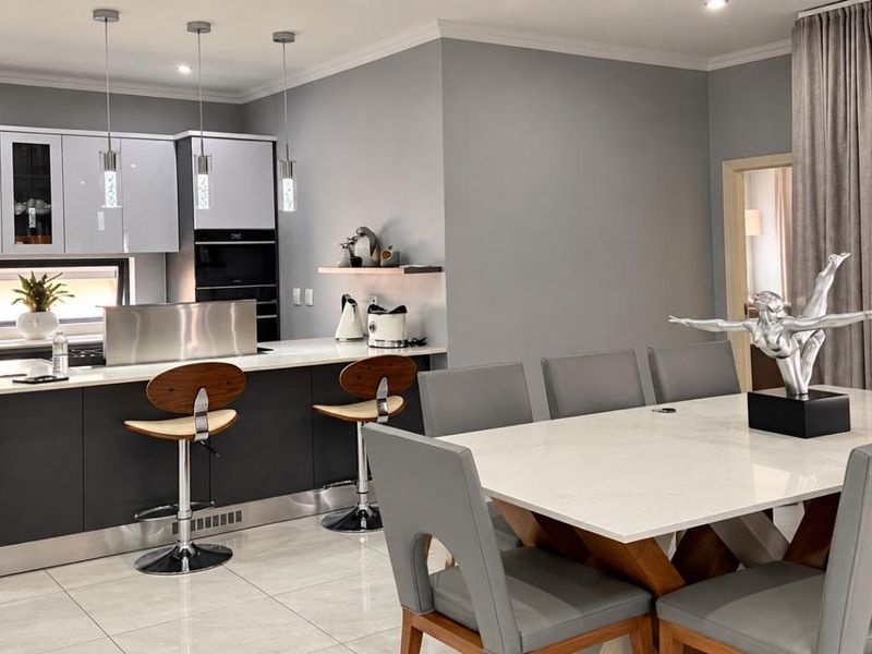 Modern open-plan kitchen and dining area featuring a sleek kitchen island, stone countertops, high-gloss cabinetry, and polished porcelain floor tiles.
