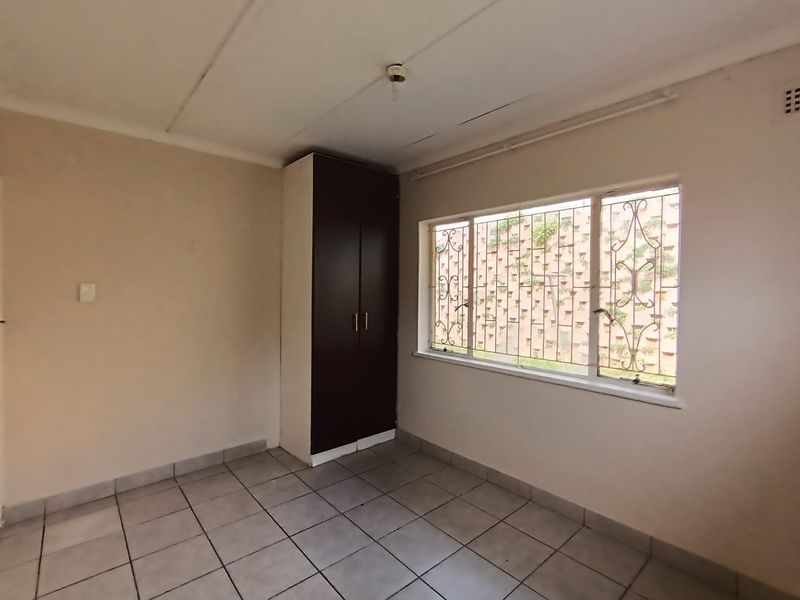 A vacant bedroom featuring tiled flooring, a built-in wardrobe, and security bars on the window.
