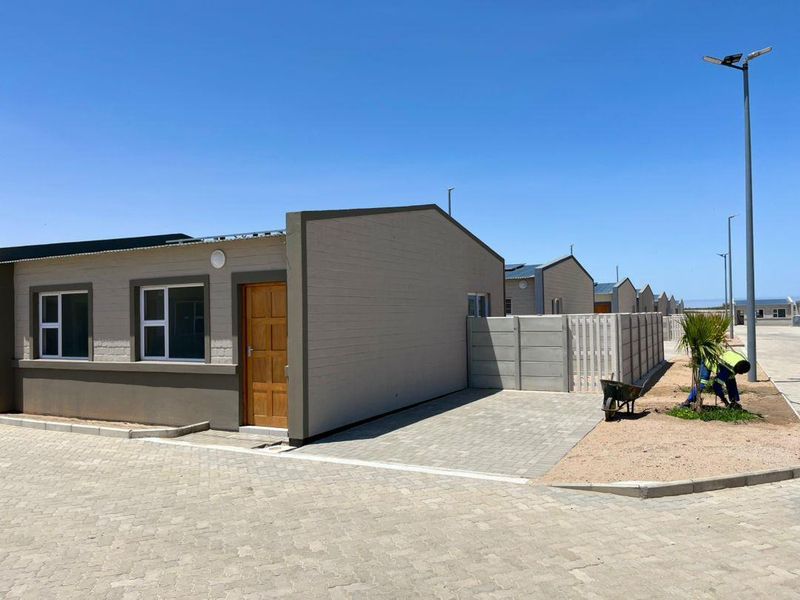 Front elevation of a modern townhouse featuring a paved driveway, timber entrance door, and secure precast concrete boundary walling.