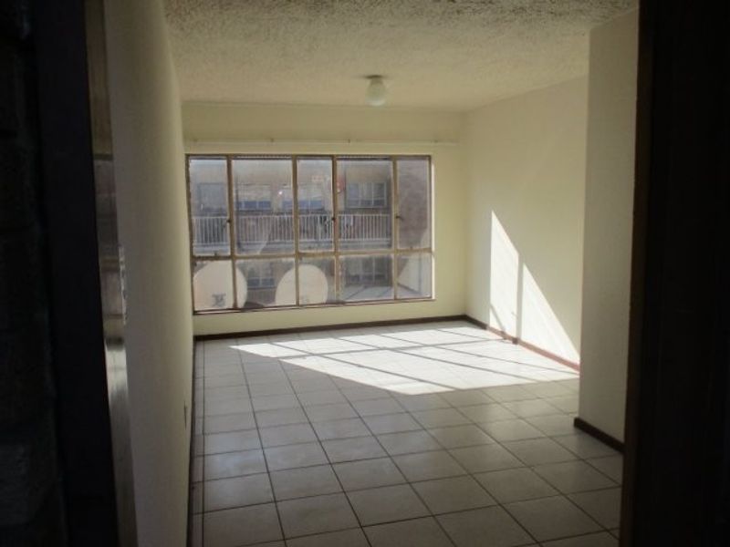 An empty, sunlit living area featuring tiled flooring and a large window, offering a blank canvas for renovation or interior design.