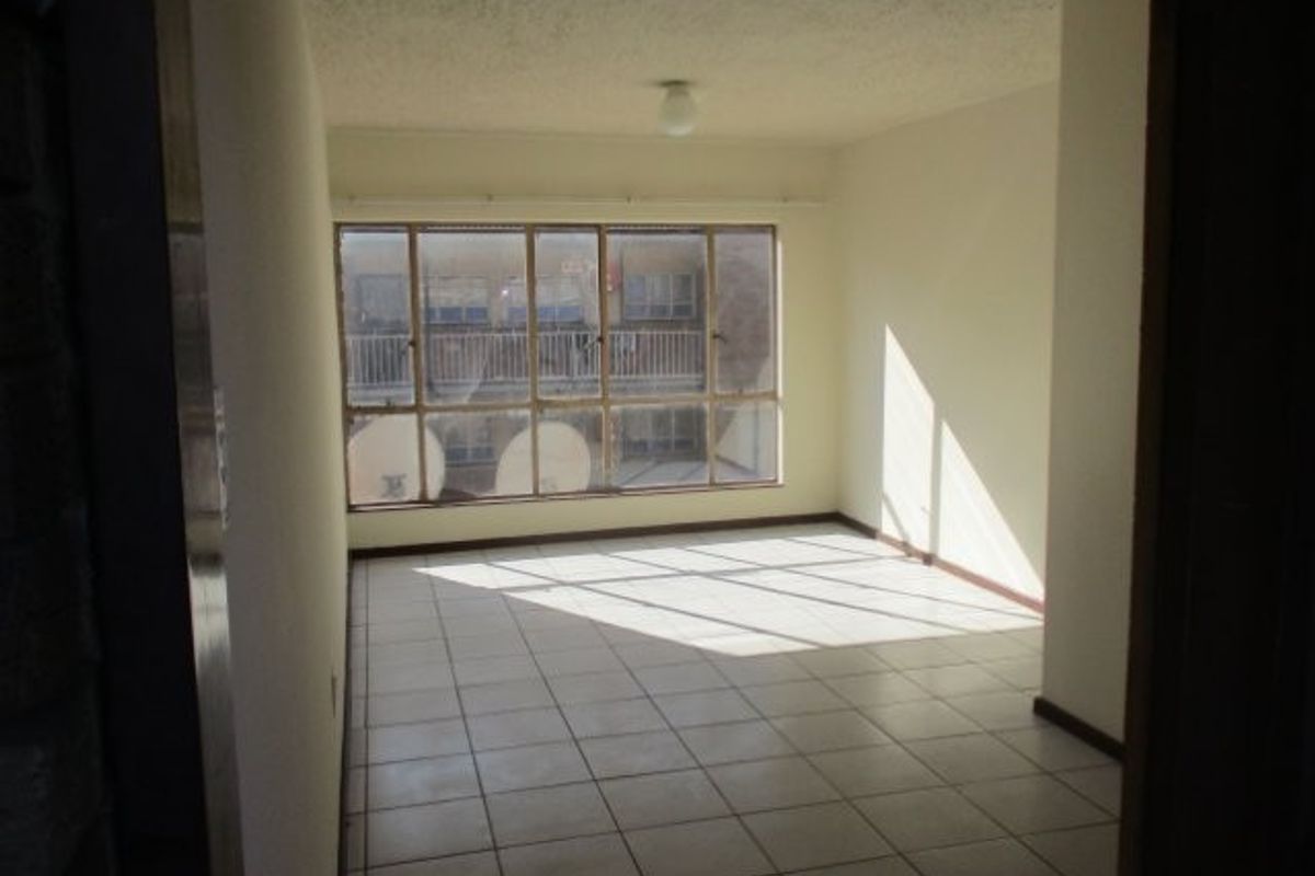 An empty, sunlit living area featuring tiled flooring and a large window, offering a blank canvas for renovation or interior design.