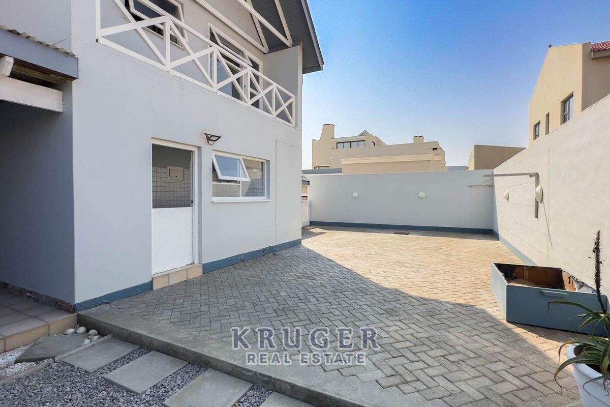 A neat, paved rear courtyard area featuring a boundary wall, external lighting, and access to the main dwelling with an overhead balcony.