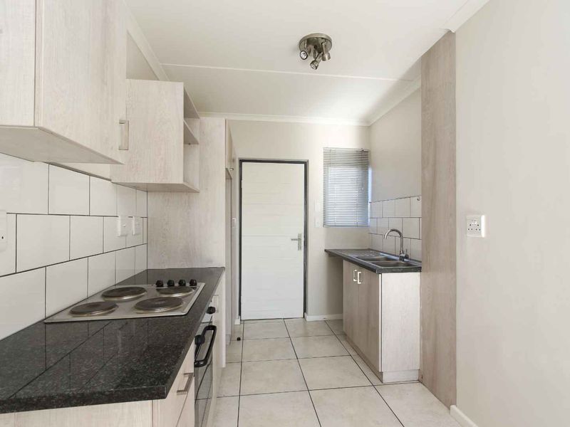 A clean, modern kitchen featuring light wood-finish cabinetry, dark granite countertops, a built-in electric hob and oven, and a double sink with tiled backsplash.