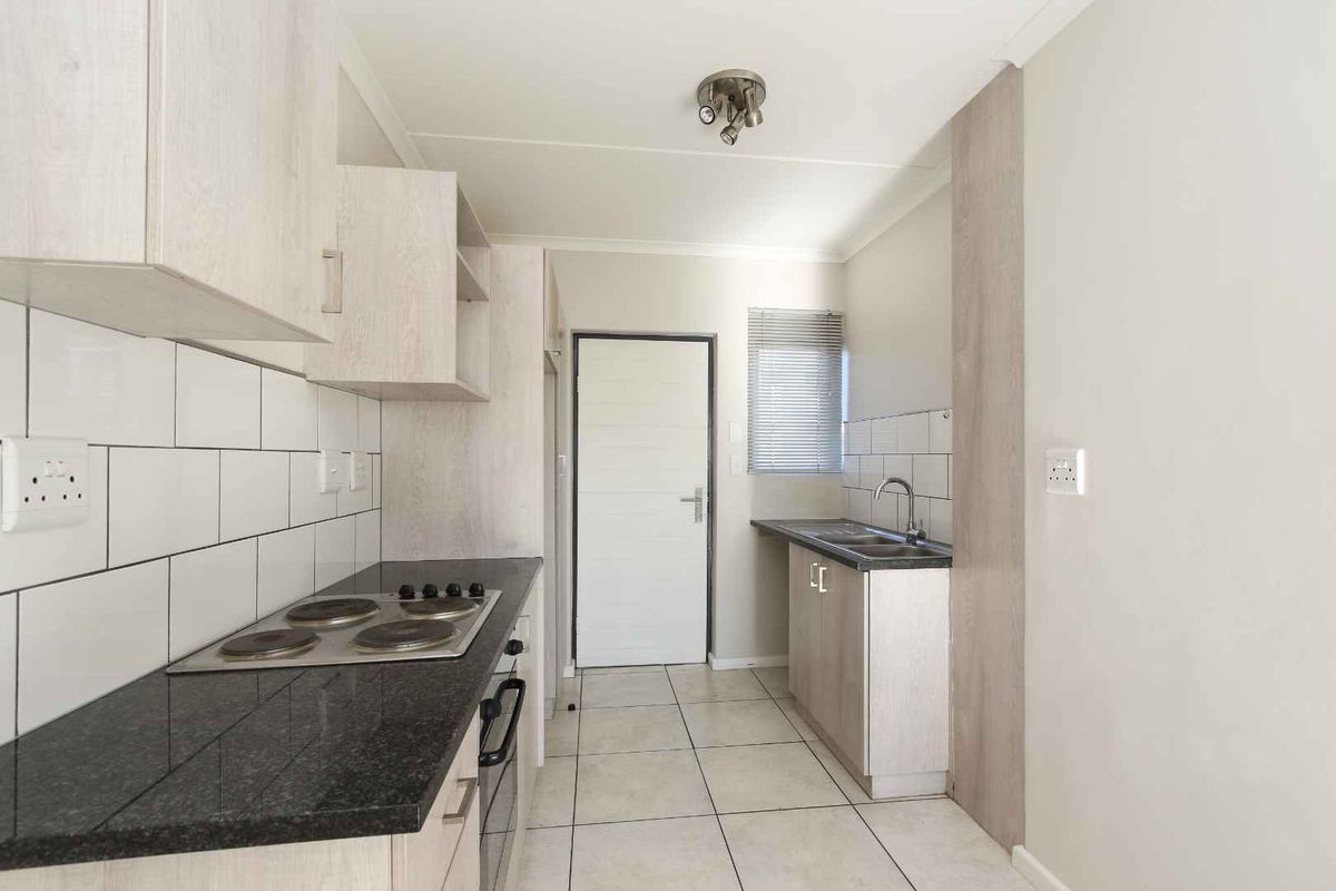 A clean, modern kitchen featuring light wood-finish cabinetry, dark granite countertops, a built-in electric hob and oven, and a double sink with tiled backsplash.