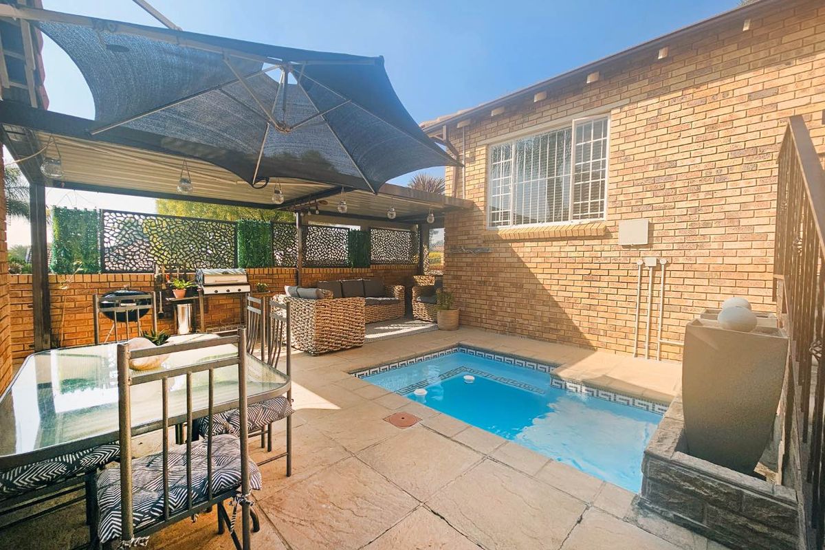 A private rear courtyard featuring a built-in swimming pool, covered patio area with shade structure, and face-brick exterior walls.