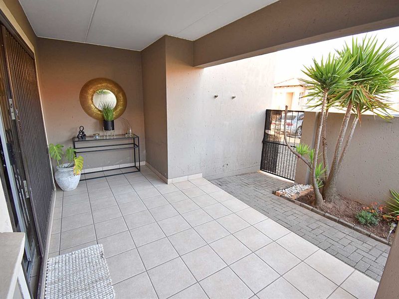 A covered patio area featuring tiled flooring, a paved walkway, and a secure metal gate, providing a functional outdoor transition space.