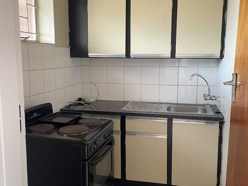 A compact, dated kitchen featuring built-in cabinetry, a stainless steel sink, tiled backsplash, and tiled flooring.