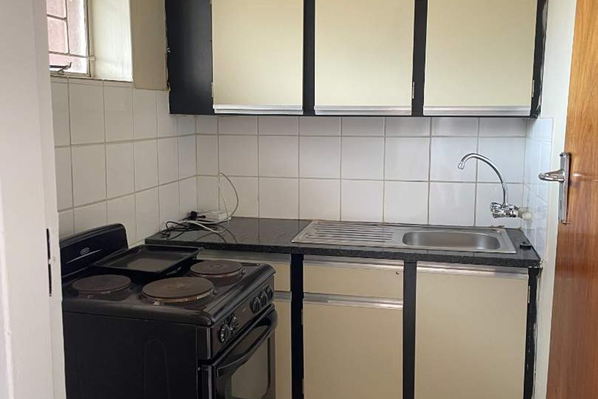 A compact, dated kitchen featuring built-in cabinetry, a stainless steel sink, tiled backsplash, and tiled flooring.