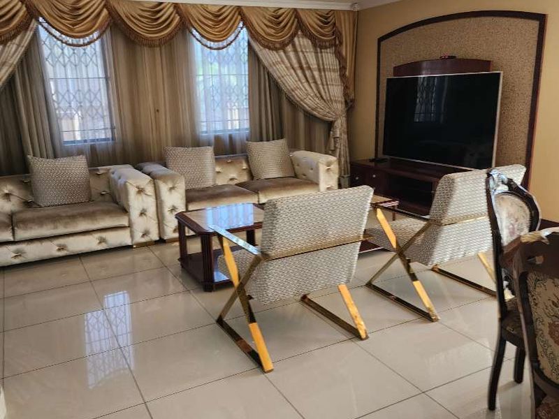 A well-maintained living room featuring polished porcelain floor tiles, recessed ceiling lighting, and a dedicated built-in media wall unit.