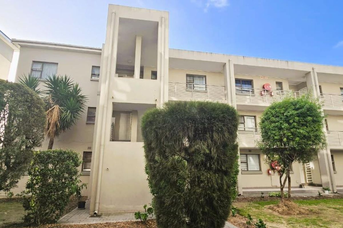 Rear view of a multi-story apartment complex featuring balconies, a central stairwell tower, and a landscaped garden area.