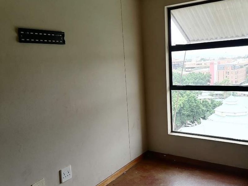 An empty bedroom featuring concrete flooring, a large window with an urban view, and wall-mounted electrical and TV connectivity points.