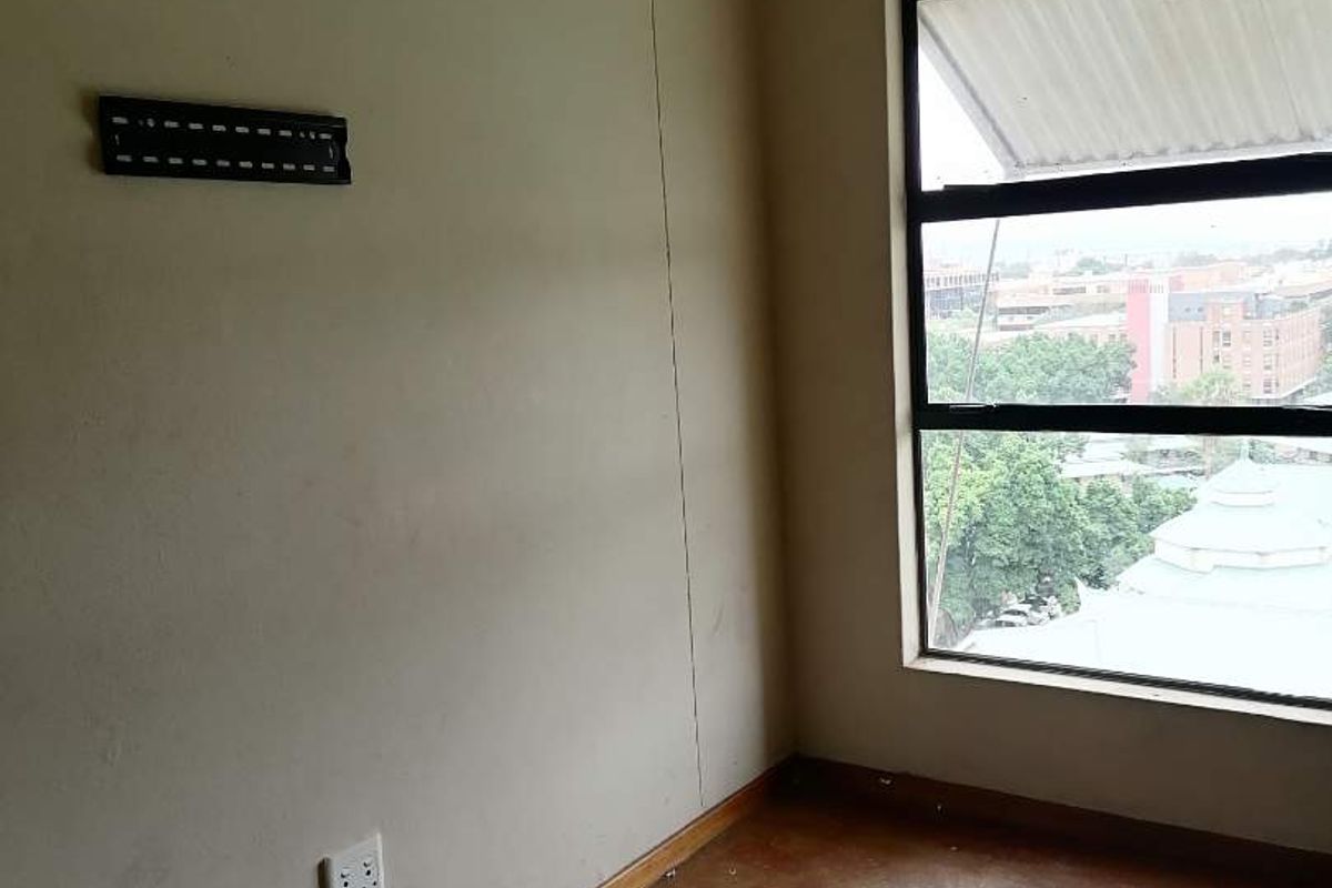 An empty bedroom featuring concrete flooring, a large window with an urban view, and wall-mounted electrical and TV connectivity points.