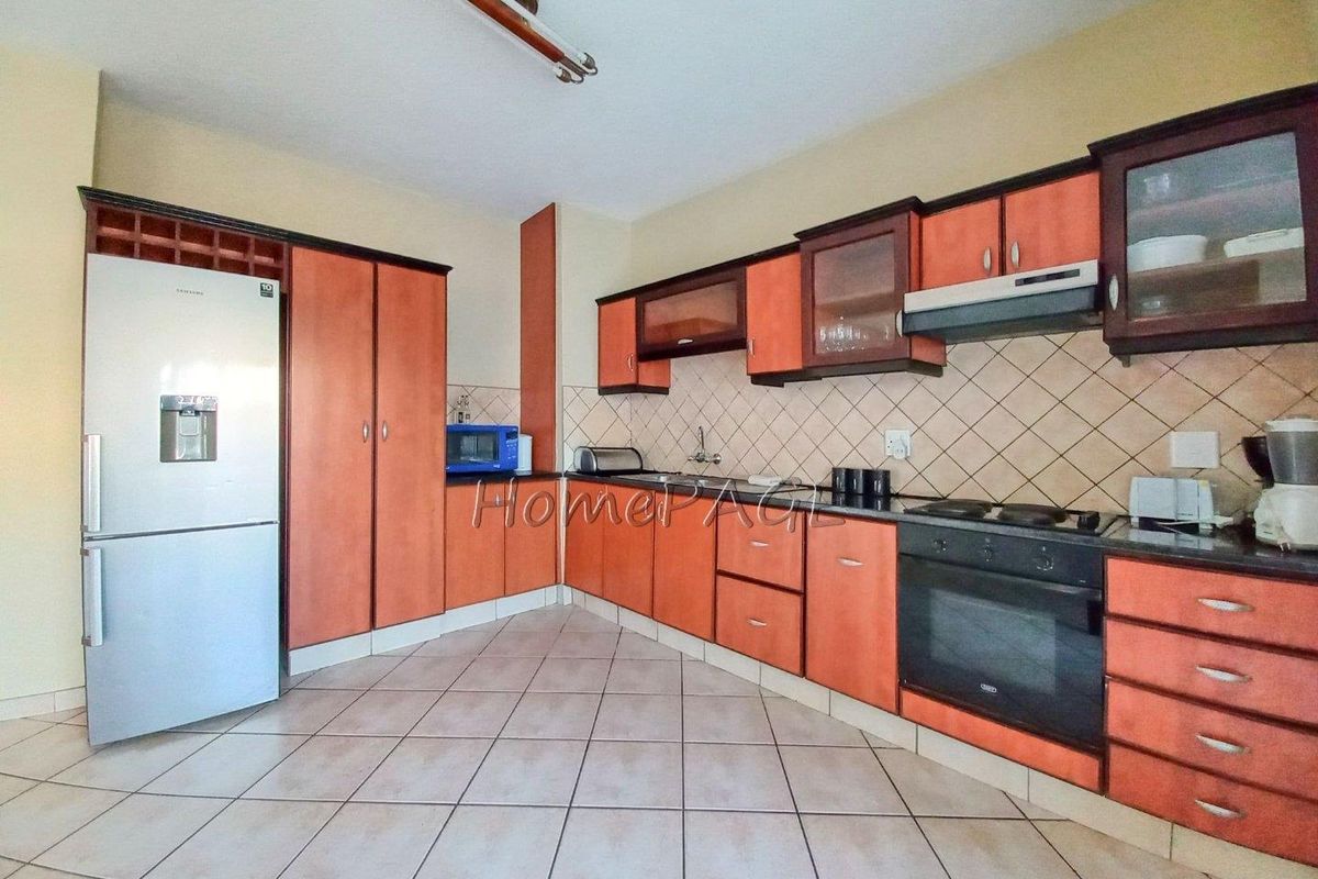 A functional kitchen featuring wooden cabinetry, tiled backsplash, built-in oven, hob, and extractor fan with tiled flooring throughout.