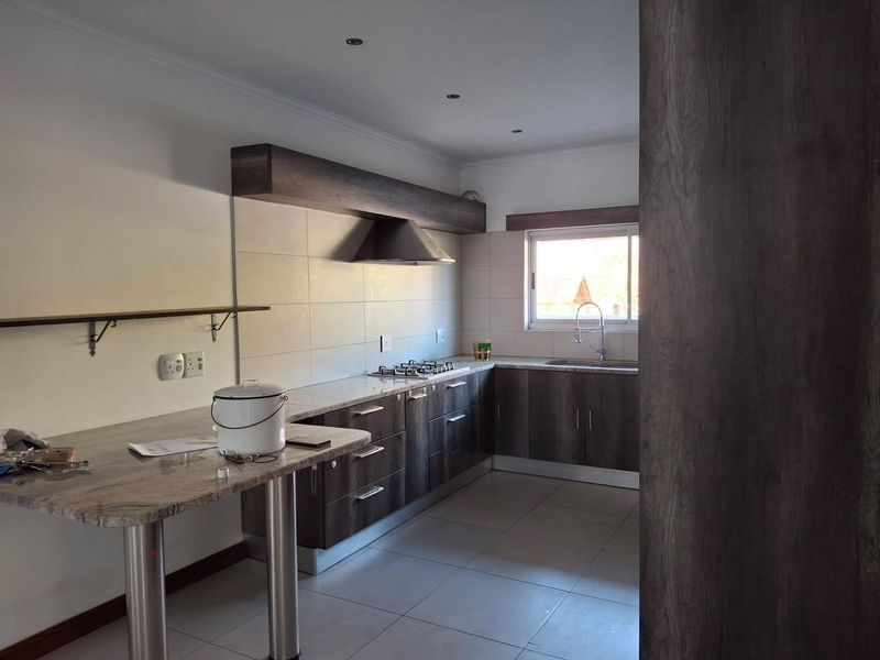 A modern kitchen featuring dark wood cabinetry, stone countertops, a gas hob with extractor fan, and tiled flooring in a clean, open layout.
