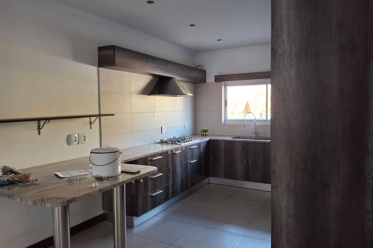 A modern kitchen featuring dark wood cabinetry, stone countertops, a gas hob with extractor fan, and tiled flooring in a clean, open layout.