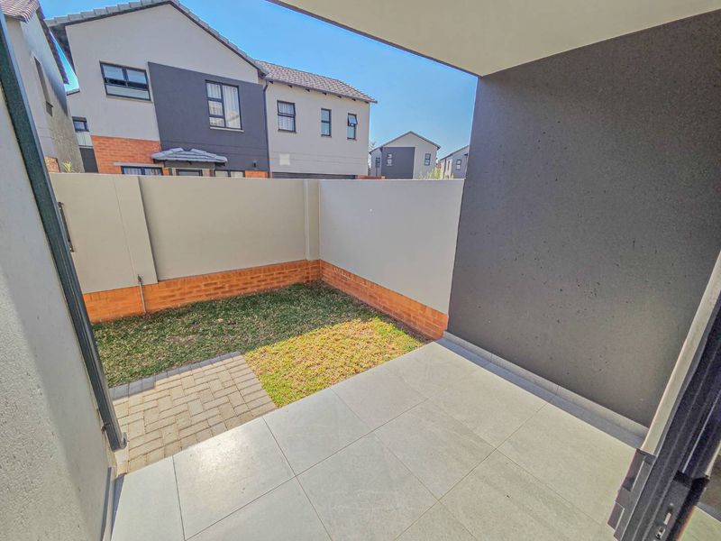 A covered patio area featuring tiled flooring, leading out to a small private garden with a paved section and brick boundary walls.