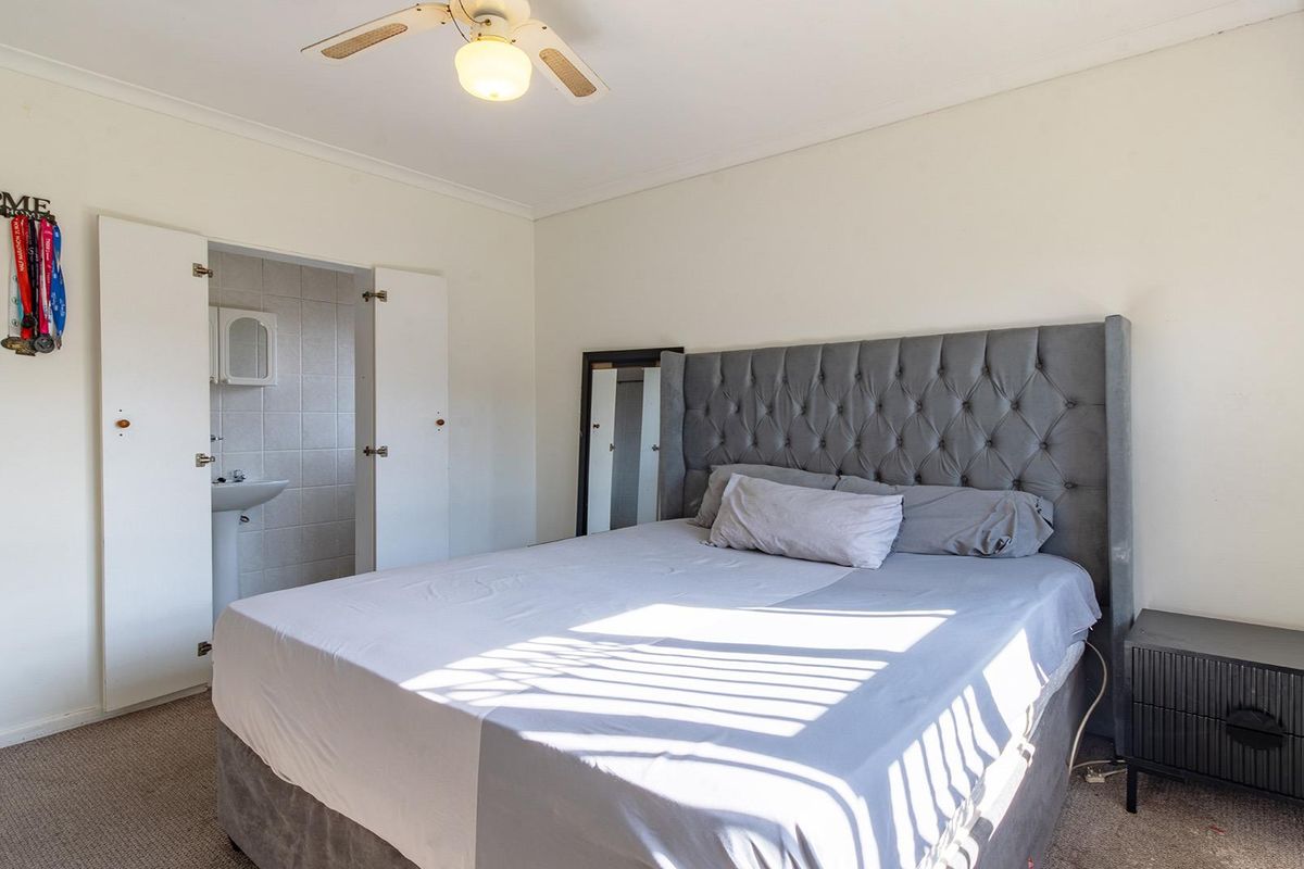 A bedroom featuring a ceiling fan, carpeted flooring, and an attached en-suite bathroom with a pedestal sink.