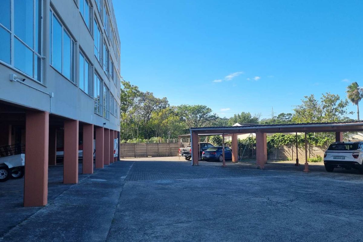 Exterior view of the apartment building showing covered parking bays and paved driveway area.