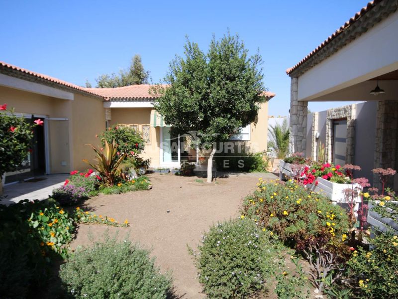A well-maintained rear courtyard garden featuring a covered patio area, stone-clad architectural details, and established garden beds.