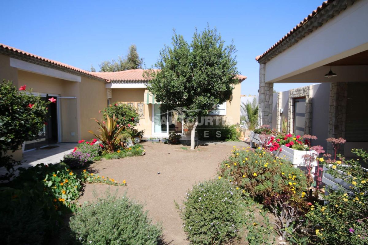 A well-maintained rear courtyard garden featuring a covered patio area, stone-clad architectural details, and established garden beds.