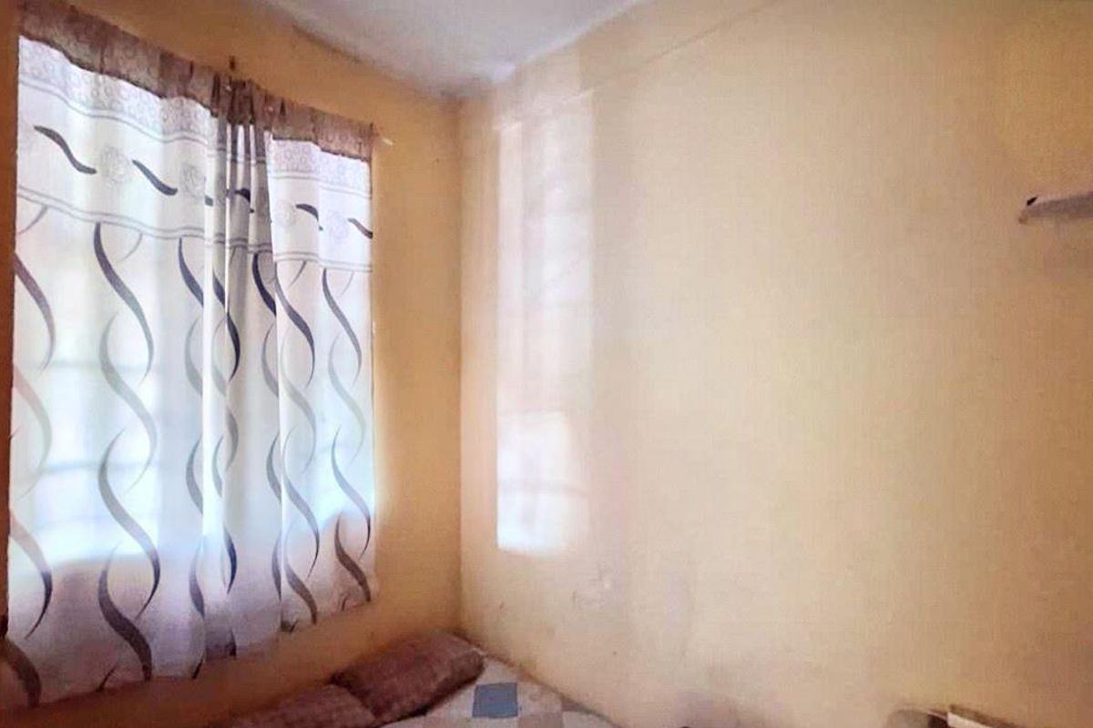 A small bedroom featuring plain walls and a window, currently in need of cosmetic updates and repairs to the wall surfaces.