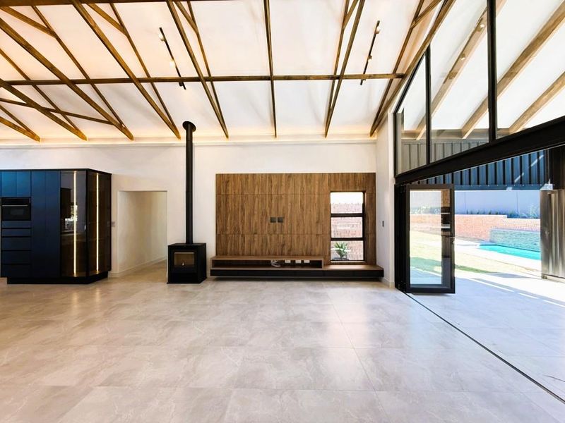 Spacious open-plan living area featuring exposed timber trusses, a modern fireplace, built-in media cabinetry, and large bi-fold doors opening to the pool area.