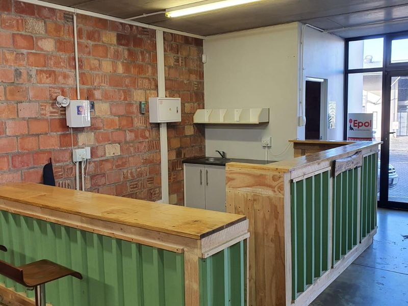 A functional utility or service area featuring an exposed brick wall, a built-in service counter, and a small kitchenette sink with direct exterior access.