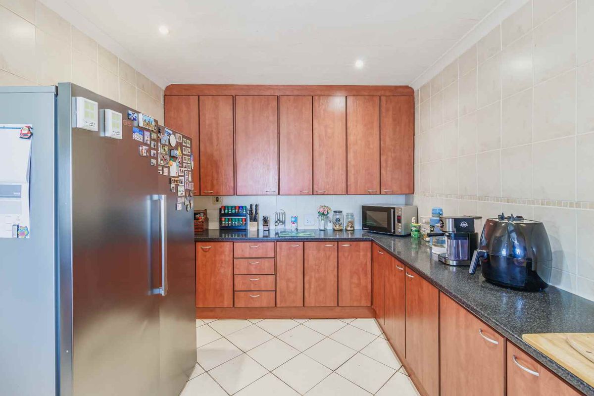 A functional kitchen featuring wood-finish cabinetry, dark granite countertops, tiled walls, and tiled flooring.