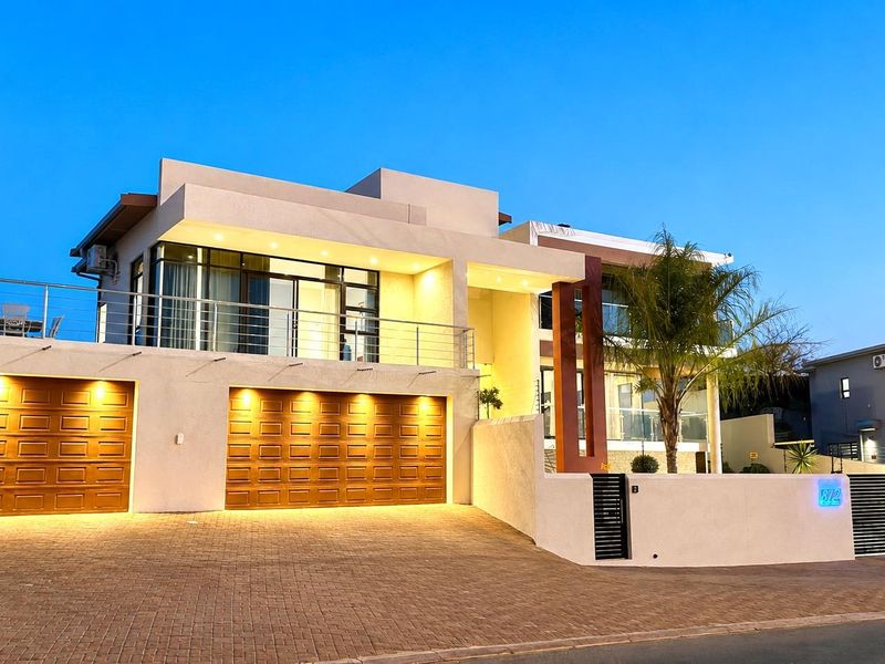 Modern double-story residence featuring a paved driveway, double garage, and an upper-level balcony with stainless steel balustrades and integrated exterior lighting.