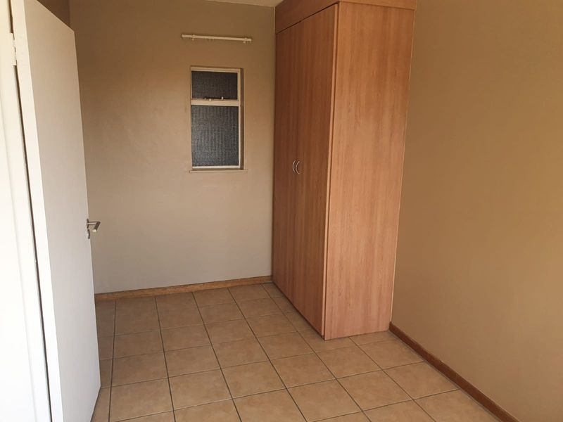 A simple, empty bedroom featuring tiled flooring, neutral wall paint, and a built-in wooden wardrobe.
