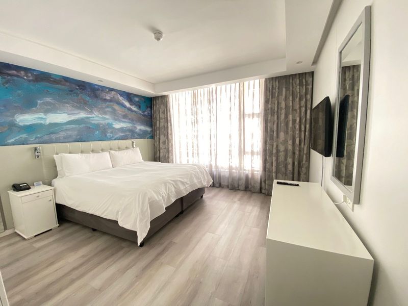 A modern, well-maintained bedroom featuring light laminate flooring, a recessed ceiling, and a wall-mounted television.