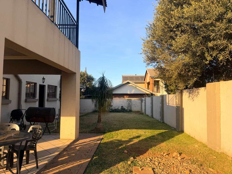 A rear exterior view featuring a covered patio area, a small lawn, and a perimeter boundary wall.