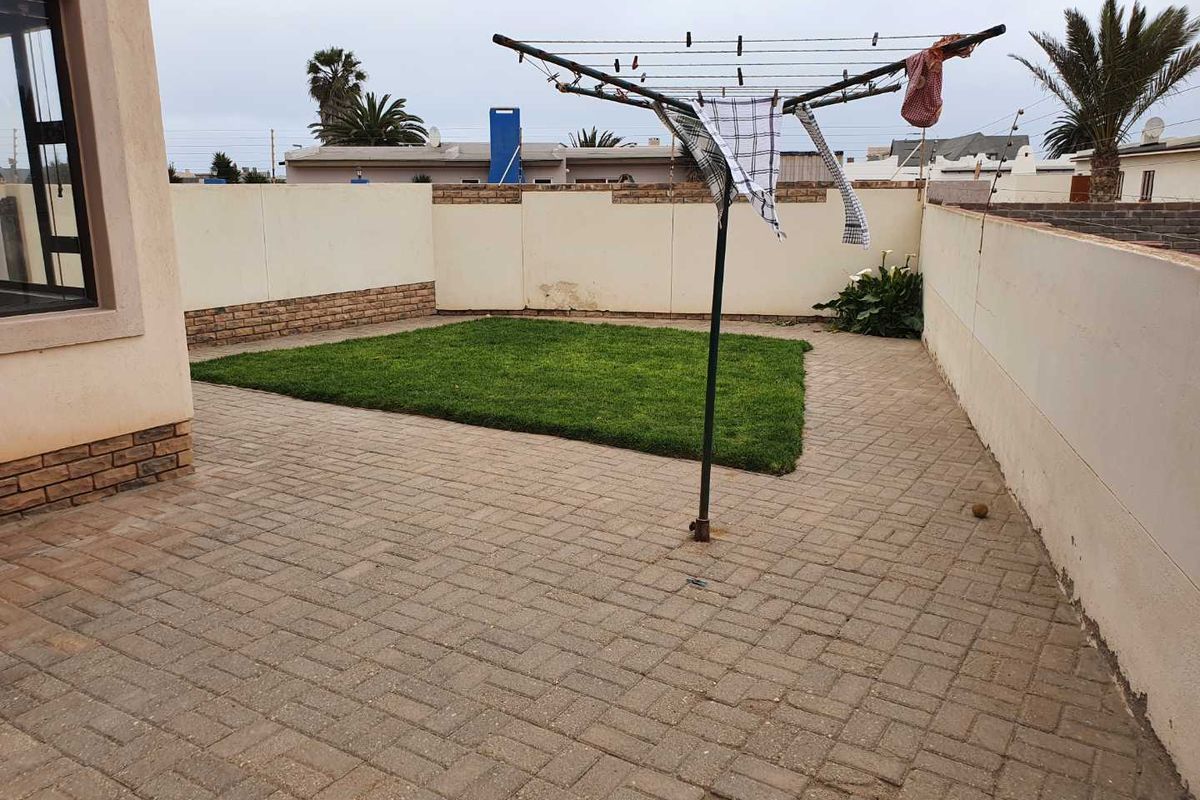 A private rear courtyard featuring paved flooring, a central grass lawn, and perimeter boundary walls.