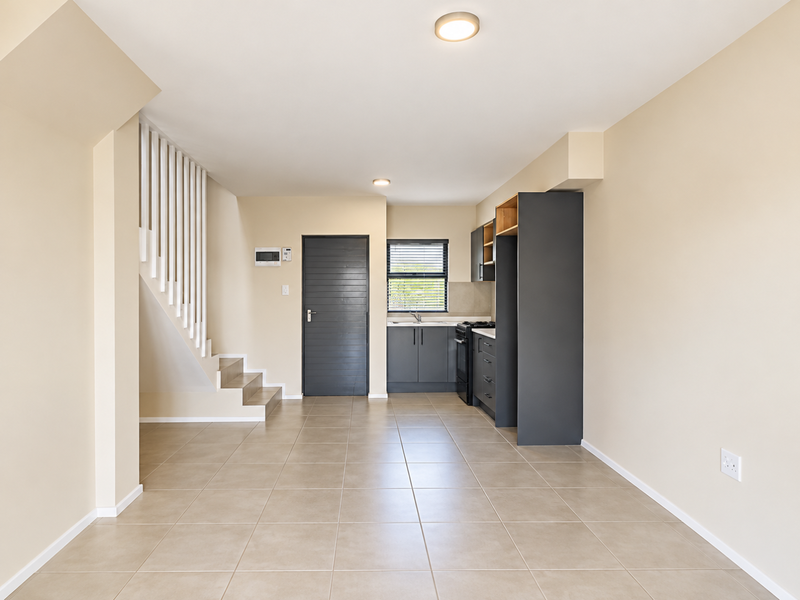 Open-plan living area featuring a modern kitchen with built-in cabinetry, tiled flooring, and an integrated staircase leading to the upper level.