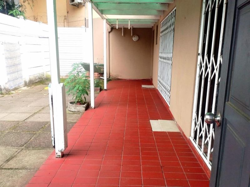 A covered outdoor patio area featuring red tiled flooring, security gates, and direct access to the rear garden space.