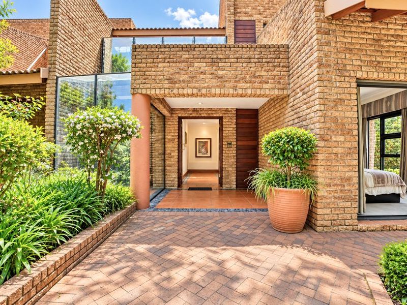 A welcoming entrance featuring a paved courtyard, face brick architecture, and a glass-walled design leading into the home.
