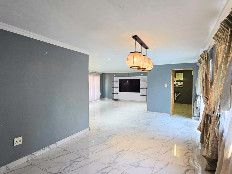 Spacious living area featuring polished marble-look floor tiles, a modern built-in media wall, and contemporary pendant lighting, offering a clean and bright open-plan layout.
