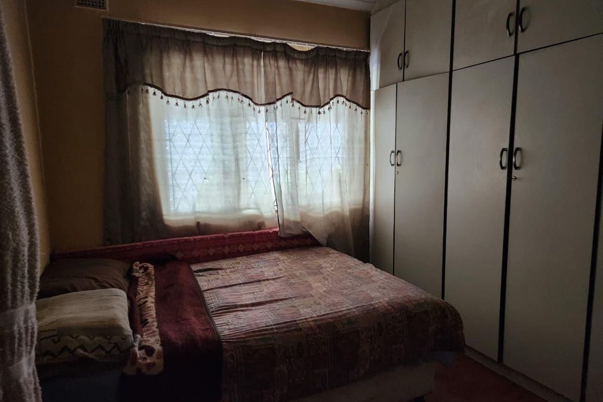 A bedroom featuring floor-to-ceiling built-in cupboards and a window fitted with security bars.