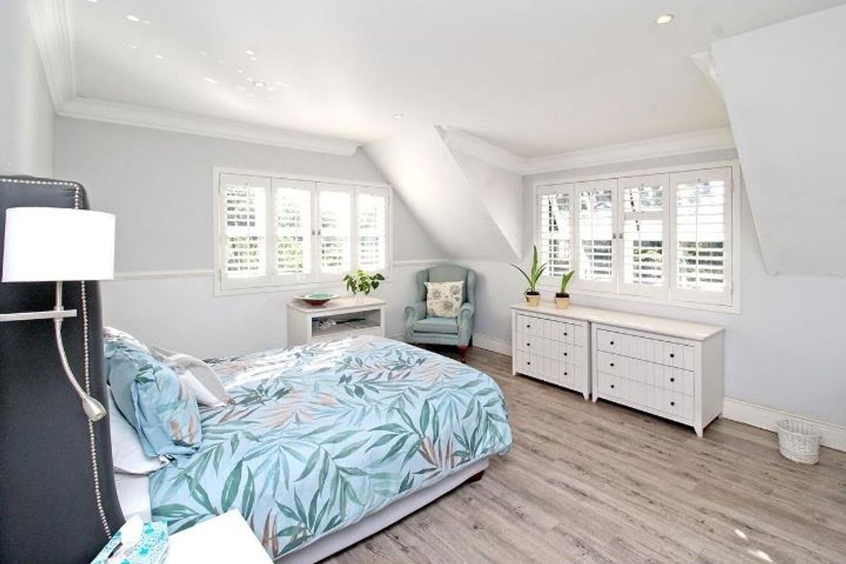 A bright and spacious bedroom featuring vaulted ceilings, wood-look flooring, and plantation shutters on the windows.