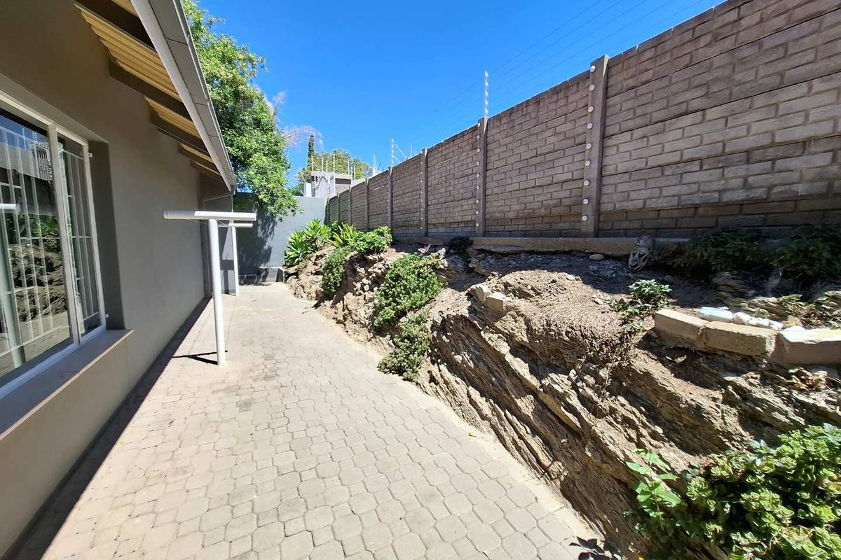 Side exterior area featuring paved walkway, rock retaining wall, and high brick boundary wall with electric fencing.
