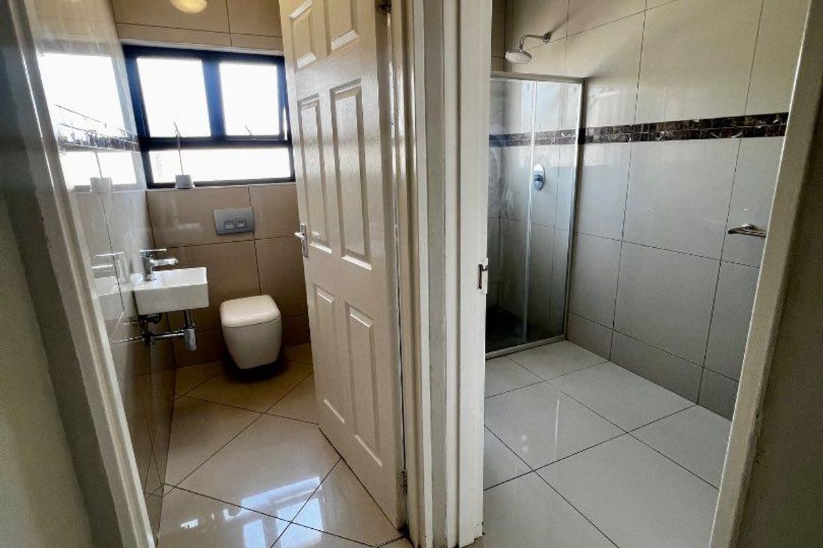 A clean, modern bathroom featuring a separate toilet area and a walk-in shower with tiled walls and floors.