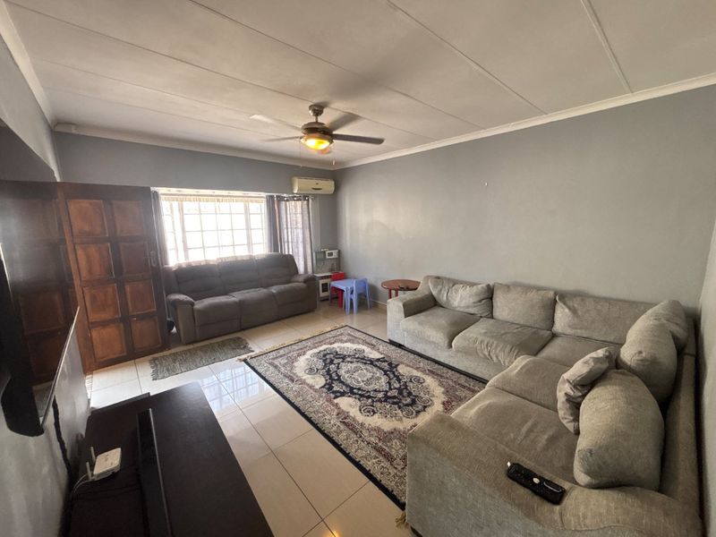 A spacious living room featuring tiled flooring, a ceiling fan, and a wall-mounted air conditioning unit, offering a comfortable and functional living space.