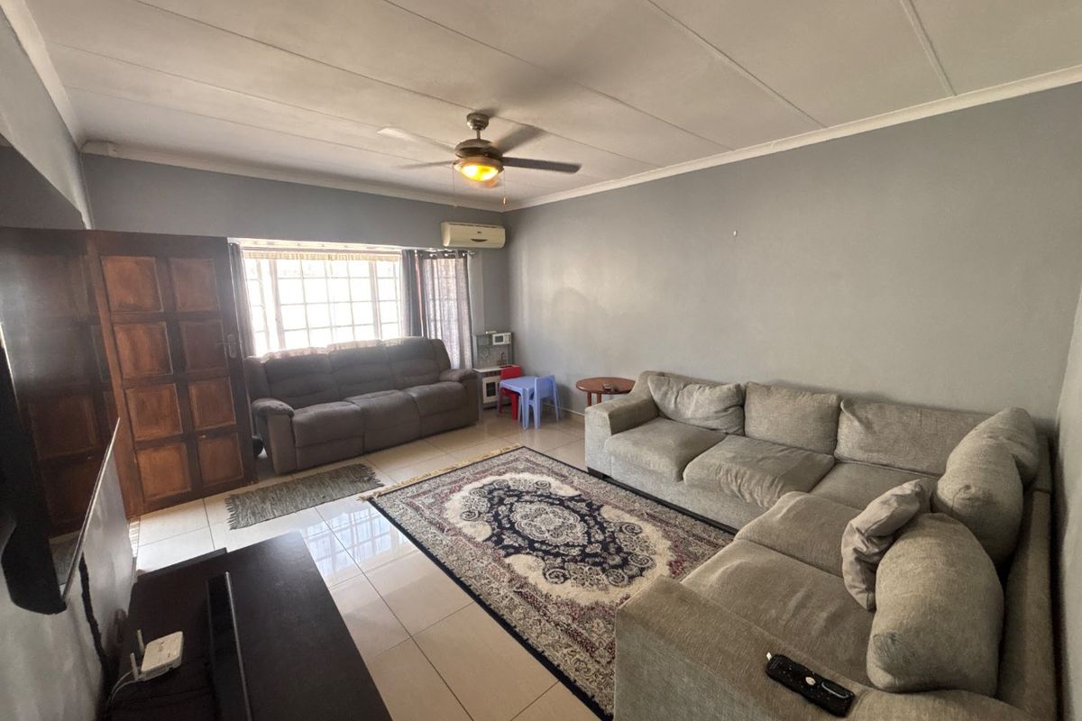 A spacious living room featuring tiled flooring, a ceiling fan, and a wall-mounted air conditioning unit, offering a comfortable and functional living space.