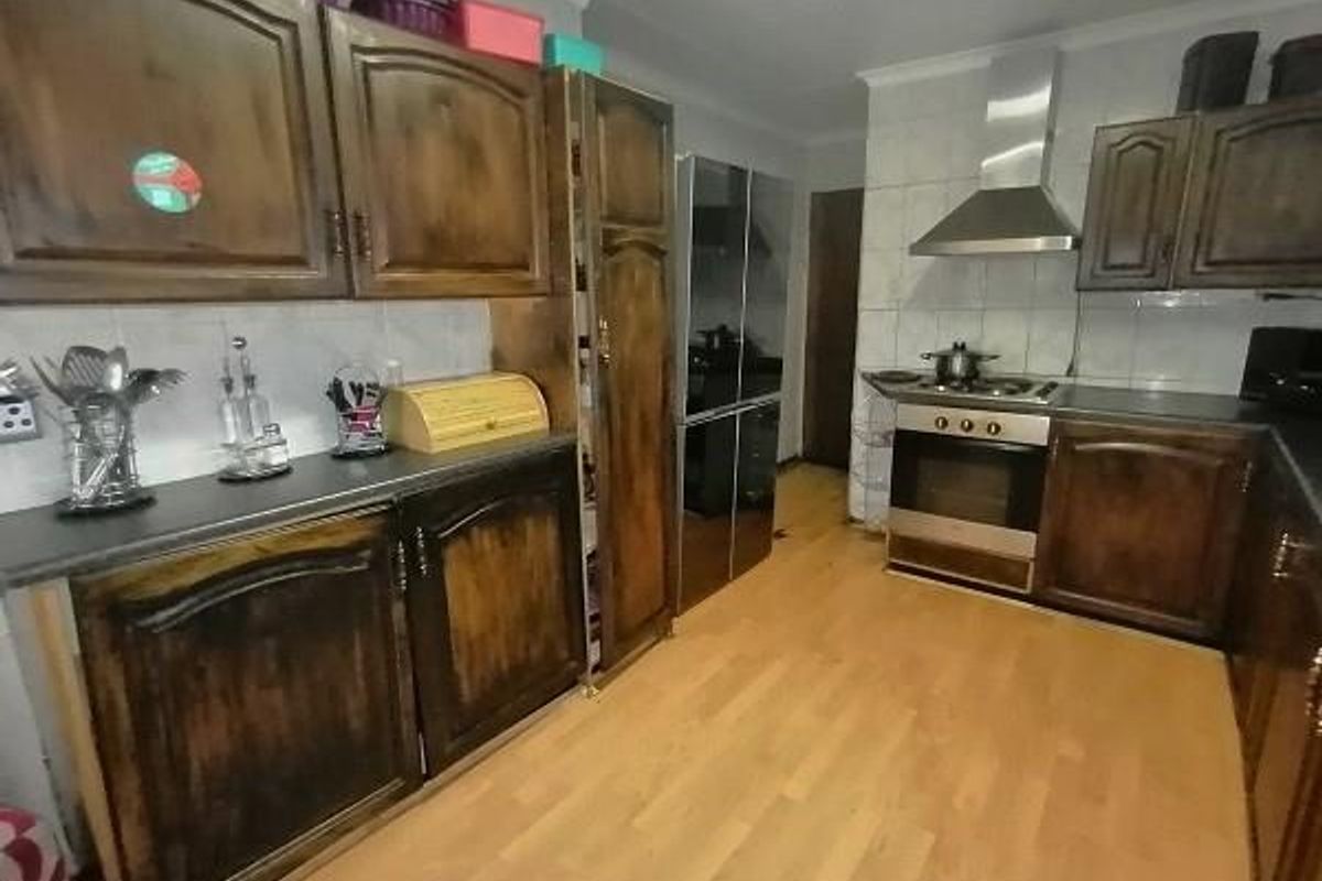 A functional kitchen featuring dark wood cabinetry, laminate flooring, a stainless steel extractor fan, and a built-in oven with a hob.