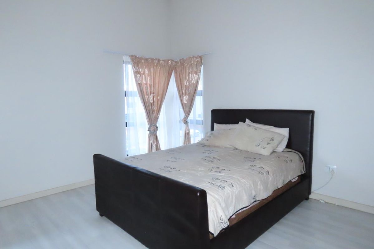 A simple bedroom featuring light-toned laminate flooring and a corner window with curtains.