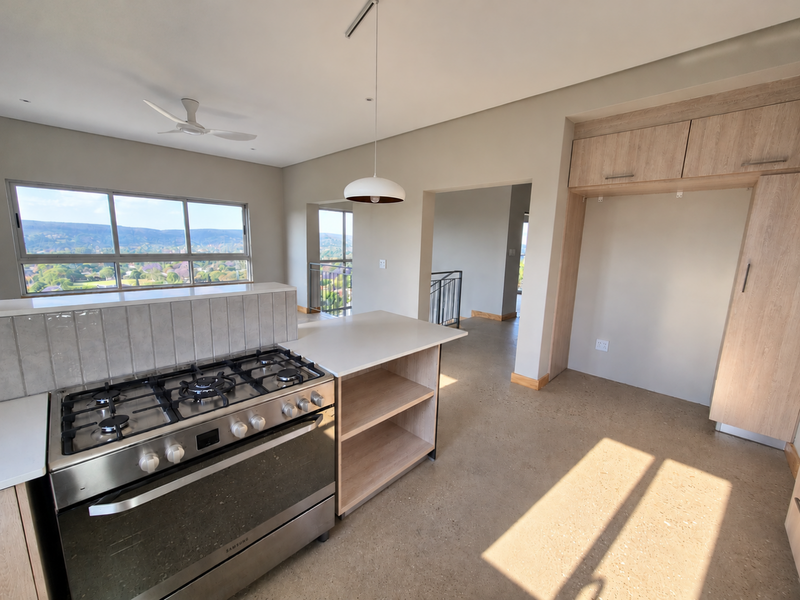 Modern kitchen featuring a gas stove, built-in cabinetry, and a central island, set against a backdrop of scenic views with polished concrete flooring.
