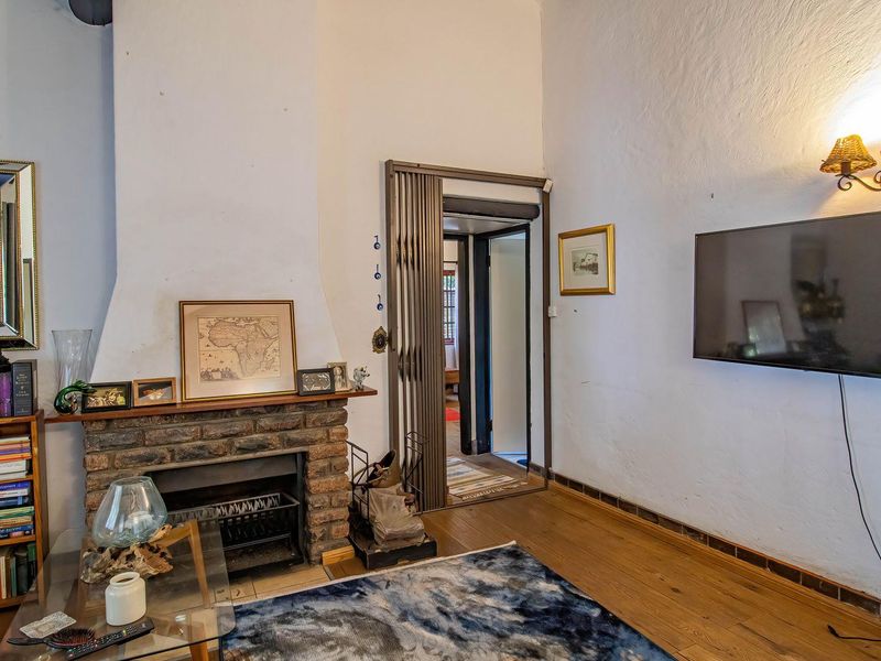 A living room featuring a rustic brick fireplace, timber flooring, and a wall-mounted light fixture, providing a cozy and traditional atmosphere.