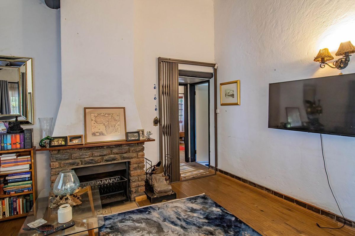 A living room featuring a rustic brick fireplace, timber flooring, and a wall-mounted light fixture, providing a cozy and traditional atmosphere.