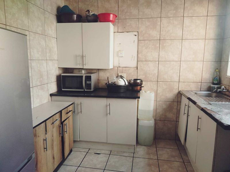 A functional kitchen featuring tiled walls, built-in cabinetry, and a stainless steel sink, currently showing signs of wear and dated finishes.
